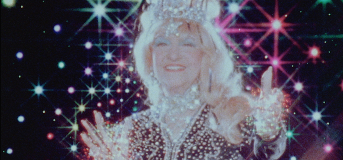 an older white woman covered in jewels, surrounded by rainbow stars.